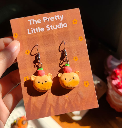 Cartoon character earrings on a 'The Pretty Little Studio' card.
